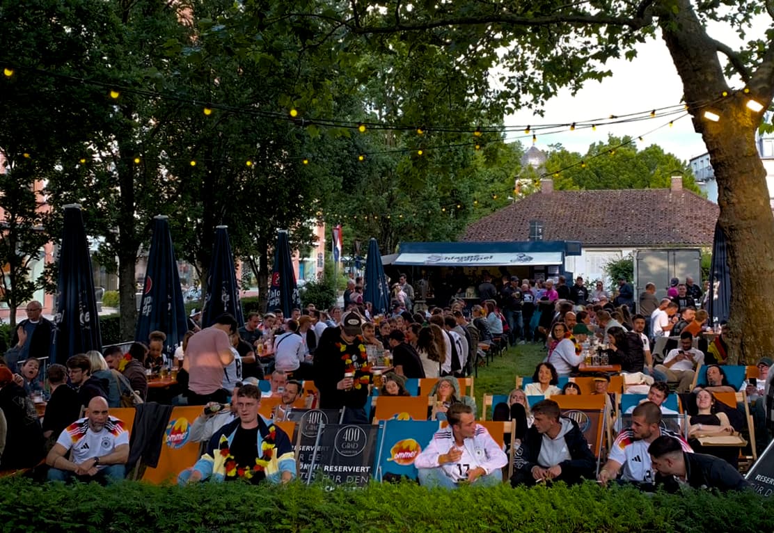 Gäste beim WM-Public-Viewing im Biergarten am Herstallturm in Aschaffenburg, Abendstimmung mit Lichterkette